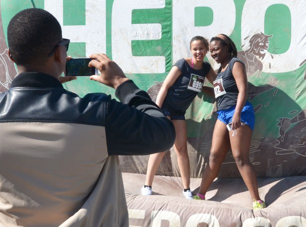 Two young women pose for the photo, being taken by a man whose back is to the viewer in this photo, before they start a race 