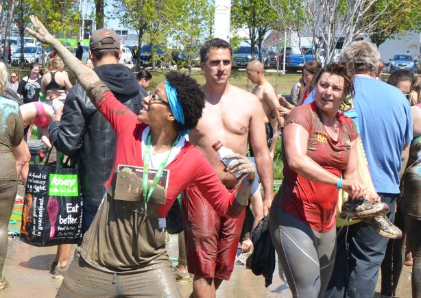 A woman covered in mud poses for a photograph while a couple of people give her strange looks. 