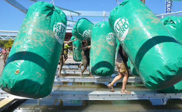 People balancing on metal beams as they walk through many punching bags, as part of an obstacle race