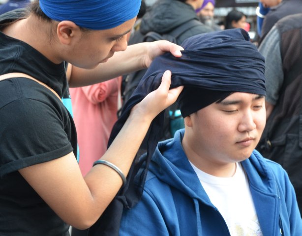 A young man having his head wrapped in a dark blue turban.  His eyes are closed.  Close up shot. 