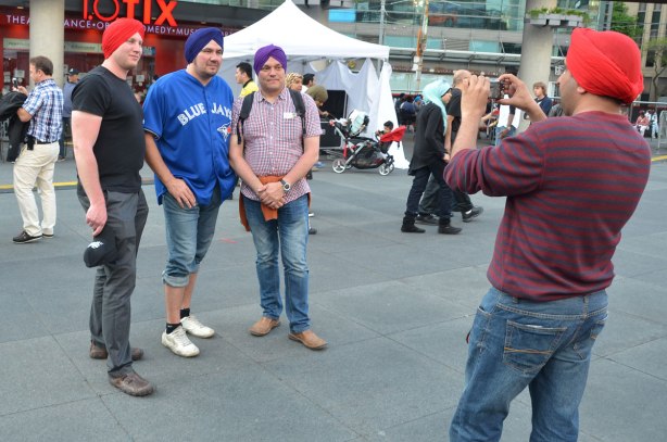 Three men in their new turbans are standing together while a fourth man is taking their picture.  