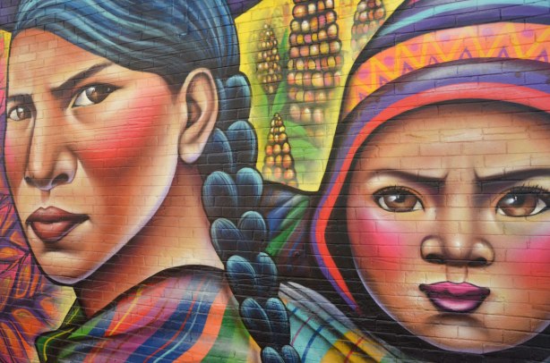 part of a large mural - a South American woman with long braided black hair with a baby wearing a Peruvian hat on her back