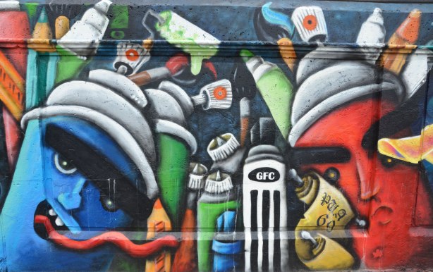 Street art painting of many cans of spray paint, some with faces on them. 