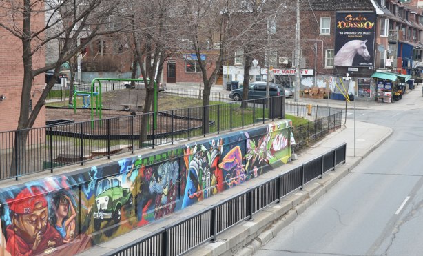 east side of mural under the railway bridge - series of street art paintings by different artists, playground behind, street scene beyond.