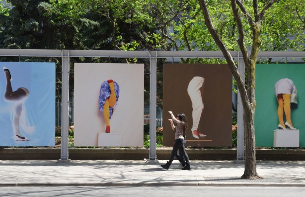 Two young women are alking past a few large, larger than life photos of legs. The women have their arms up in the air.