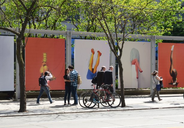 people in front of 4 large photos of legs by Isabelle Wenzel. A couple are saying goodbye, two men in suits are walking together, a woman is looking at the pictures as she walks past and another woman is walking out of the photo on the right.