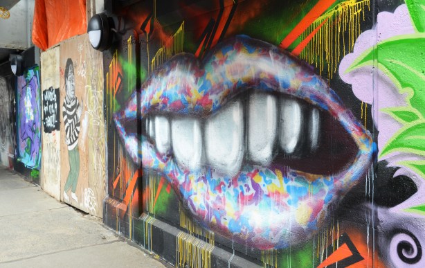 street art painting under a railway bridge - big multicoloured lips, partially open revealing big white teeth