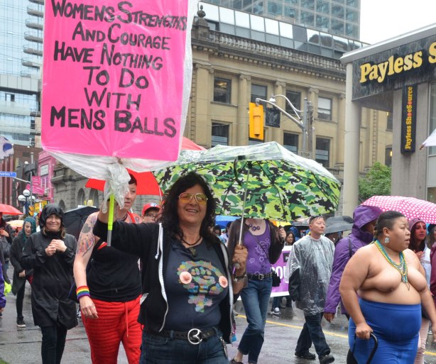 Pride week, Dyke march, a woman is carrying a pink sign that says "womens strength and courage has nothing to do with mens balls"