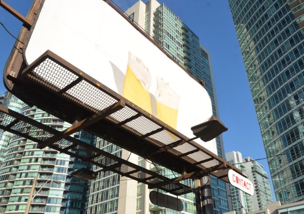 a billboard above a parking lot, condos in the background.   A pair of yellow rubber gloves with the openings turned into a cuff are all that in the image on the board
