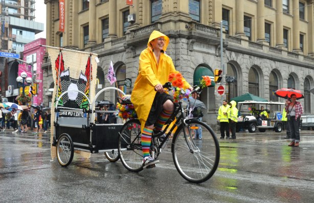 pride dyke march, dykes on bikes, woman in bright yellow raincoat rides a bicycle that is pulling a trailer