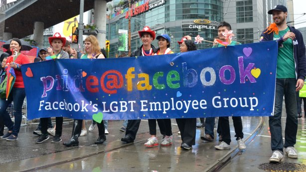 group of people holding up a blue banner that says Facebooks LGBT employee group