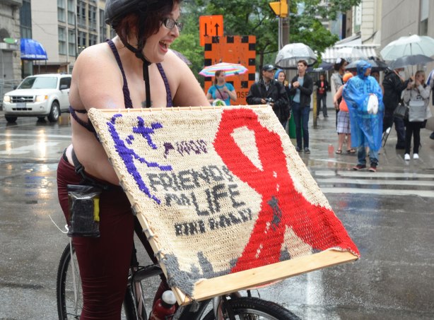 pride week, dyke march, woman on a bike is holding a sign with a red AIDS ribbon and the words 'friends for life'