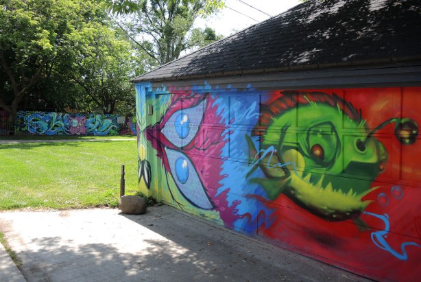 in the foreground is a garage with two pieces of street art, a little green monster on a red background, and half a butterfly