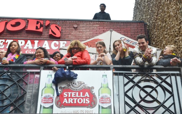 people at a pride parade on a rainy day - a group watches the parade from the balcony of a bar 