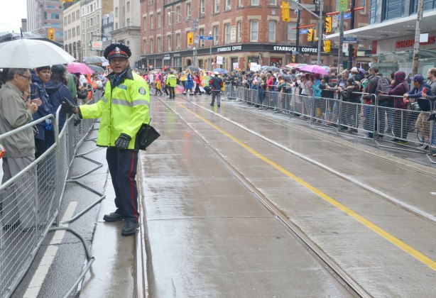 people at a pride parade on a rainy day - a policeman helps with crowd control along the barricades of the parade route 