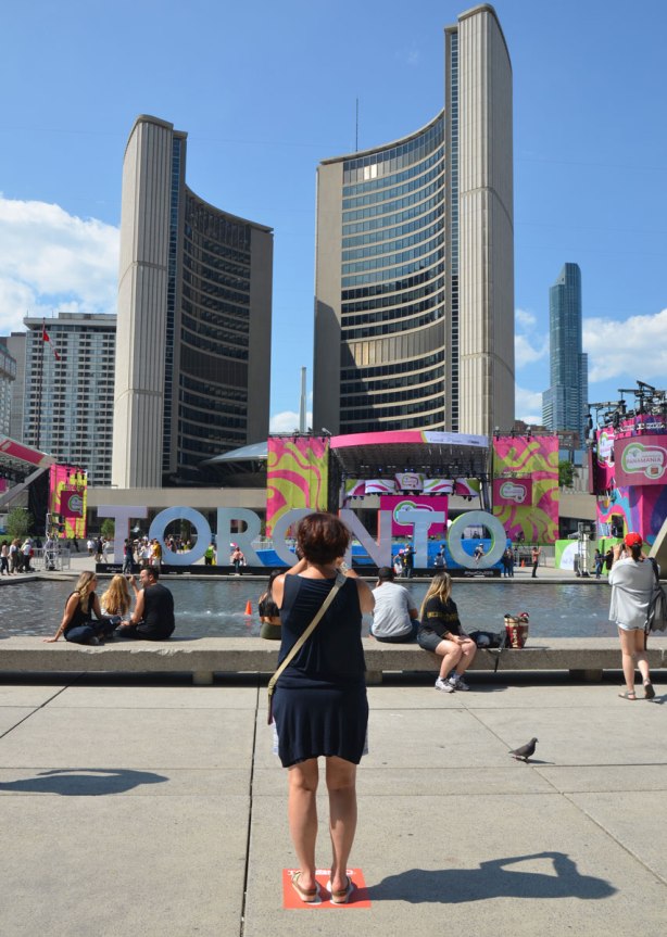 large three dimensional block capital letters that spell Toronto installed alongside the pool fountain in Nathan Phillips Square - a woman stands with her back to the camera and takes a picture