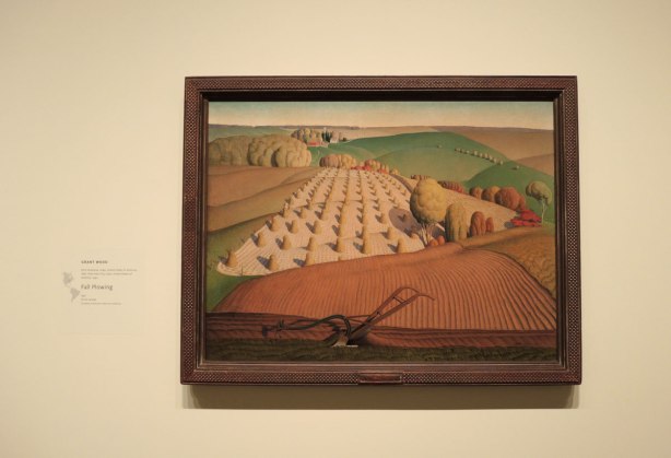 painting on a wall in an art gallery of fields being harvested by Grant Wood