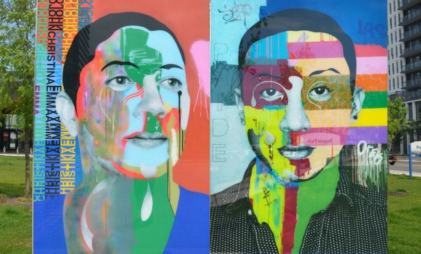 on a concrete plaza at the entrance to a park, large glass laminate artwork that is a colourful portrait of a person - two men, the one on the right has the word pride written into the painting