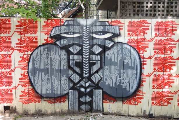graffiti and street art in Graffiti Alley in Toronto - a wooden gate, double doors, so that when the doors are closed a stylized face is the result.  It has mirror symmetry. 