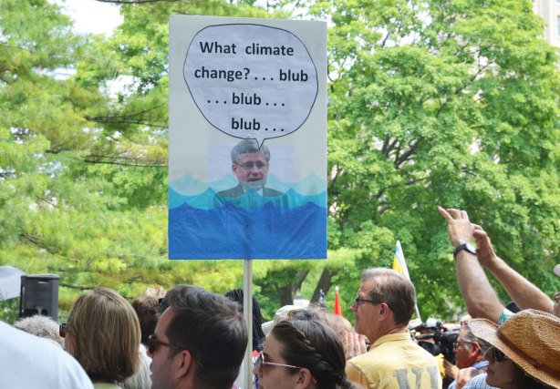 A group of people at a protest rally.  Somone is holding up a sign with a picture of Stephen Harper neck deep in water with the words, 'What climate change blub blub blub'