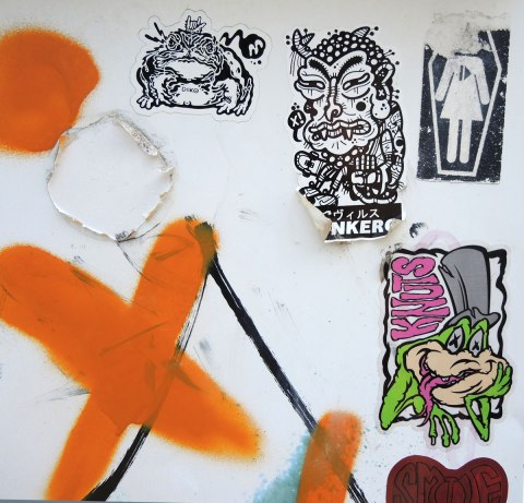 graffiti and street art in Graffiti Alley in Toronto - five stickers on white, also a big orange X.  One sticker is a knuts frog with its tongue stuck out. 