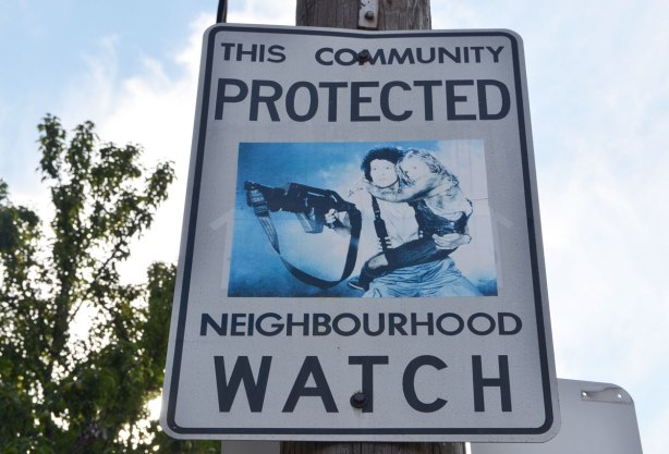Neighbourhood watch sign with picture of Sigourney Weaver as Ellen Ripley in 'Aliens, carrying a child and a very big gun
