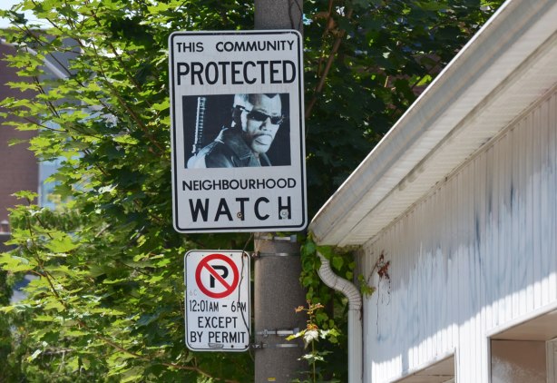 An altered Neighbourhood Watch sign. A picture of a black man wearing sunglasses and with a machine gun on his back