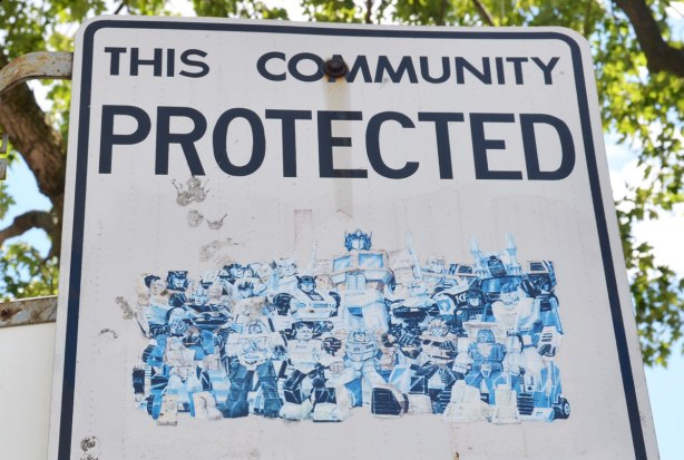 An altered Neighbourhood Watch sign. A faded picture of a large group of transformers, the superheros from the old TV series.