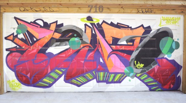 graffiti and street art in Graffiti Alley in Toronto - a colourful tag on a white garage door.  The number 710 is above the door. 