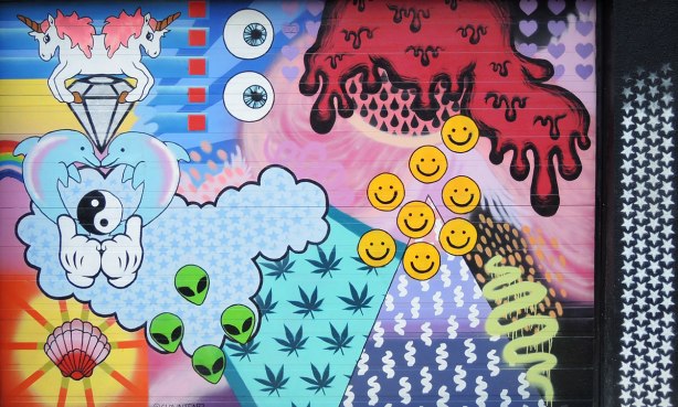 graffiti and street art in Graffiti Alley in Toronto - a collage like piece of street art on a garage door by clowntearz.  Googley eys, cannabis leaves, happy faces, zigzags, green  alien faces, red ooze