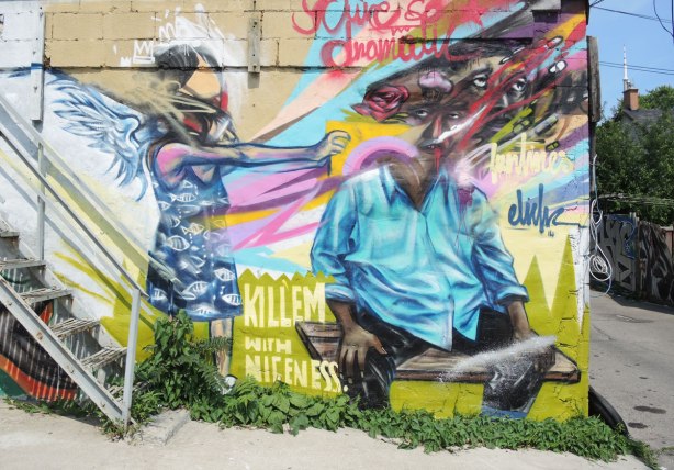 graffiti and street art in Graffiti Alley in Toronto - on a wall at the bottom of the stairs, a mulitfaced person by elicser with a woman standing beside him with her arms stretched towards him.  The words 'Kill'em with niceness' are written between the couple 