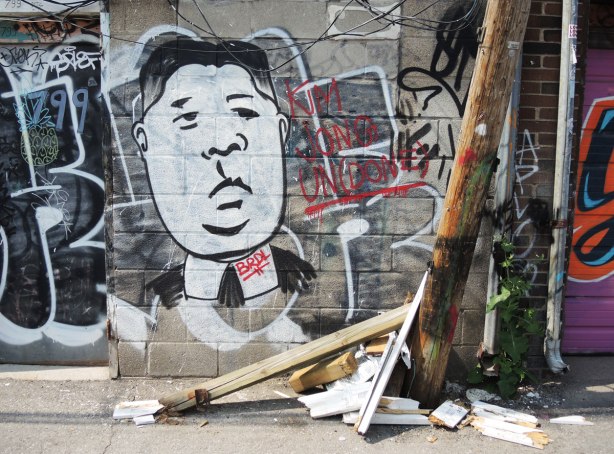 graffiti and street art in Graffiti Alley in Toronto - A large white man's face on a garage door, with a pile of broken boards in front of it.  The man is supposed to be Kim Jong of North Korea 