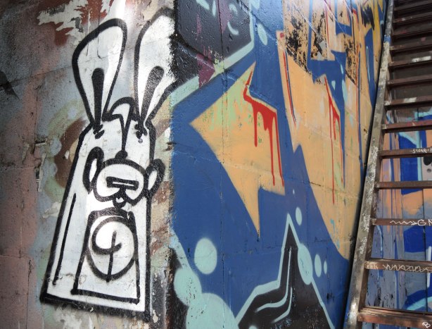 a black and white poser bunny on a wall at the corner, around the corner is a painted arrow that is part of a graffiti painting