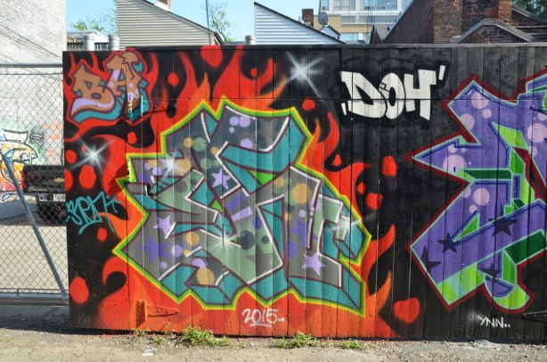 tags on a black wall in an alley. Between them is the word doh