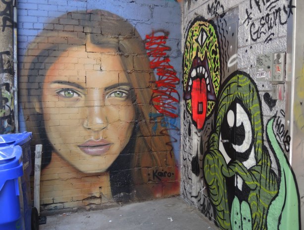 Woman's face painted by Kairo in an alley, blue background