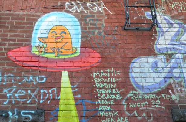 uber 5000 birdie in a little space ship with a beam of light eminating from the bottom, on a red brick wall