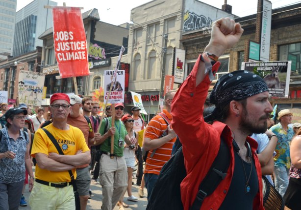 A man in a red shirt pumps his fist in the air as he walks in a protest march