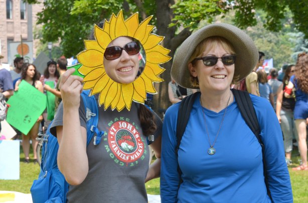 At a protest rally, two women are posing for a picture.  One has a large cut out around her face that makes her face look like a large yellow flower