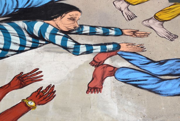 a street artist painting of a woman in a blue and white striped shirt flying with her arms outstretched.  Two pairs of feet as well as a pair of hands belonging to other people are also in the picture. 