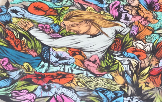 street artist painting of a woman with long yellow hair emerging from a bed of flowers.