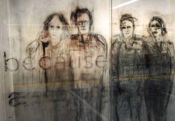 part of an art installation, paintings on glass panels, a group of people standing. The word because is also visible in the picture