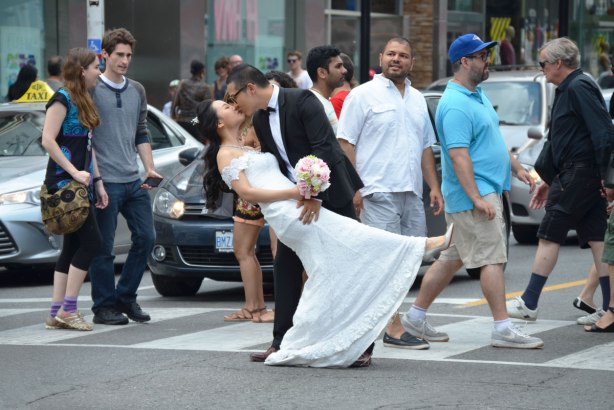 The bridegroom in his black suit dips the bride in her white wedding dress in the middle of a pedestrian crossing across Yonge St. at Dundas in TOronto. 