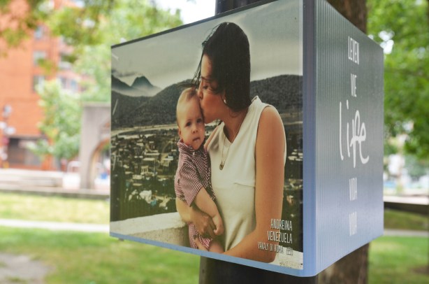 poster on a lamp post with the picture of a mother and her son. Park is in the background. Part of an exhibit in association with the Pan Am Games.