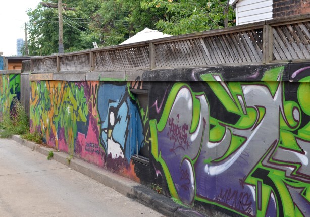 a fence that runs down the right side of an alley has been covered with street art 