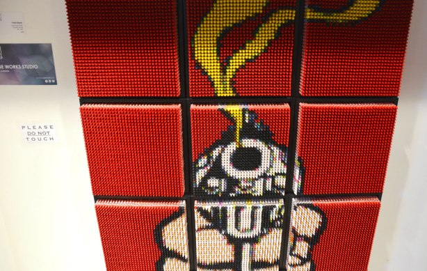 An image of a smoking revolver that is pointed at the viewer. It is made from 9 squares and each square is filled with crayons on their ends. The background is red crayons, the smoke is yellow crayons.