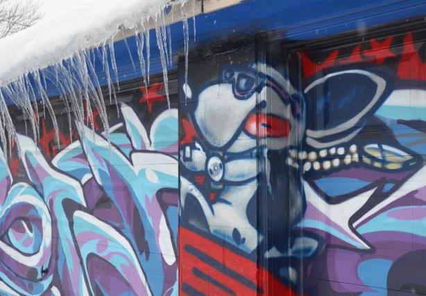 street art of a dog wearing sunglasses and pretending to be a pilot, taken in the winter as there are icicles hanging from the roof