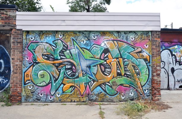A garage door in an alley covered with a street art painting of letters and hand grenades - spud bombs