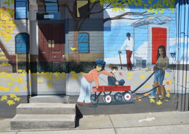 part of mural that depicts a street scene - two kids are playing on a red wagon, a woman is walking a dog and a woman with a cane is waiting at a bus shelter. 