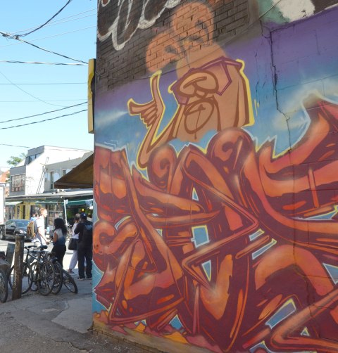 a poser bunny street art painting at the corner of a building is in the foreground, people on Kensington Ave are in the background 
