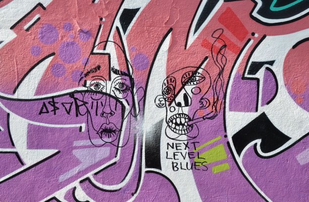 Graffiti Alley - two black line drawings of faces that have been drawn on top of a pink and purple street art painting. 